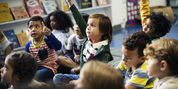 Kinder, die im Kindergarten auf dem Boden sitzen und die Hände hochhalten
