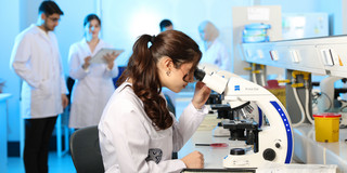 Young female scientist is examining samples under a microscope in a modern lab.. 