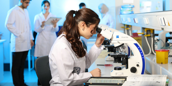 Junge Wissenschaftlerin untersucht Proben unter einem Mikroskop in einem modernen Labor.