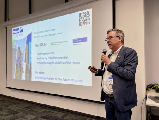 Marcio Weichert präsentiert Folien mit einem Mikrofon in der Hand