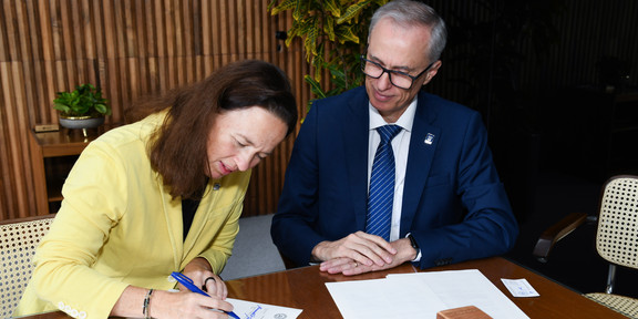 Prof. Maximiliane Wilkesmann (TU Dortmund) und UFMG-Rektor Alessandro Fernandes Moreira sitzen an einem Tisch und unterzeichnen die Vereinbarung.