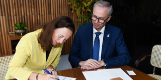 Prof. Maximiliane Wilkesmann (TU Dortmund) und UFMG-Rektor Alessandro Fernandes Moreira sitzen an einem Tisch und unterzeichnen die Vereinbarung.